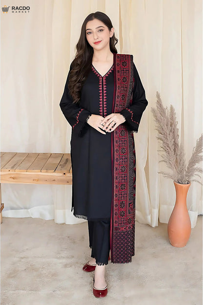 Woman wearing a black and red traditional outfit with a patterned scarf, standing in a room with a wooden bench and vase.

