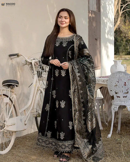 Woman in a black embroidered traditional outfit standing next to a white bicycle outdoors.

