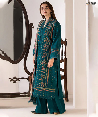 Woman wearing a teal embroidered outfit in a minimalistic setting

