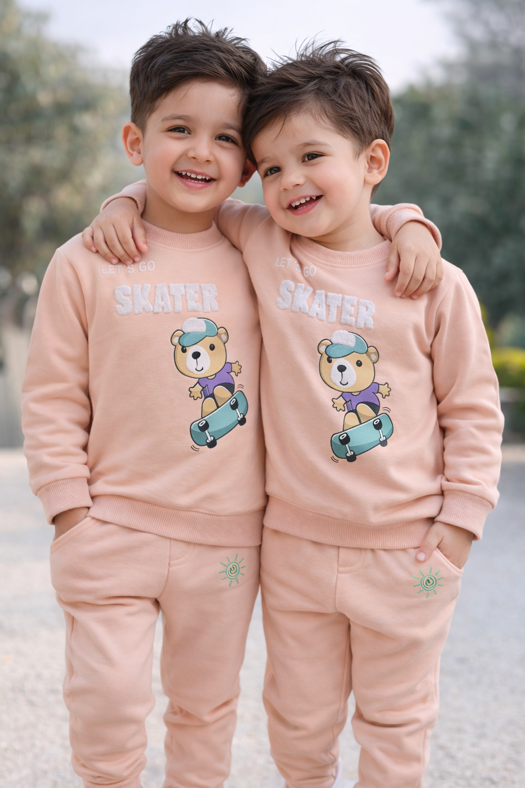 Two children wearing matching pink outfits with teddy bear graphics outdoors.


