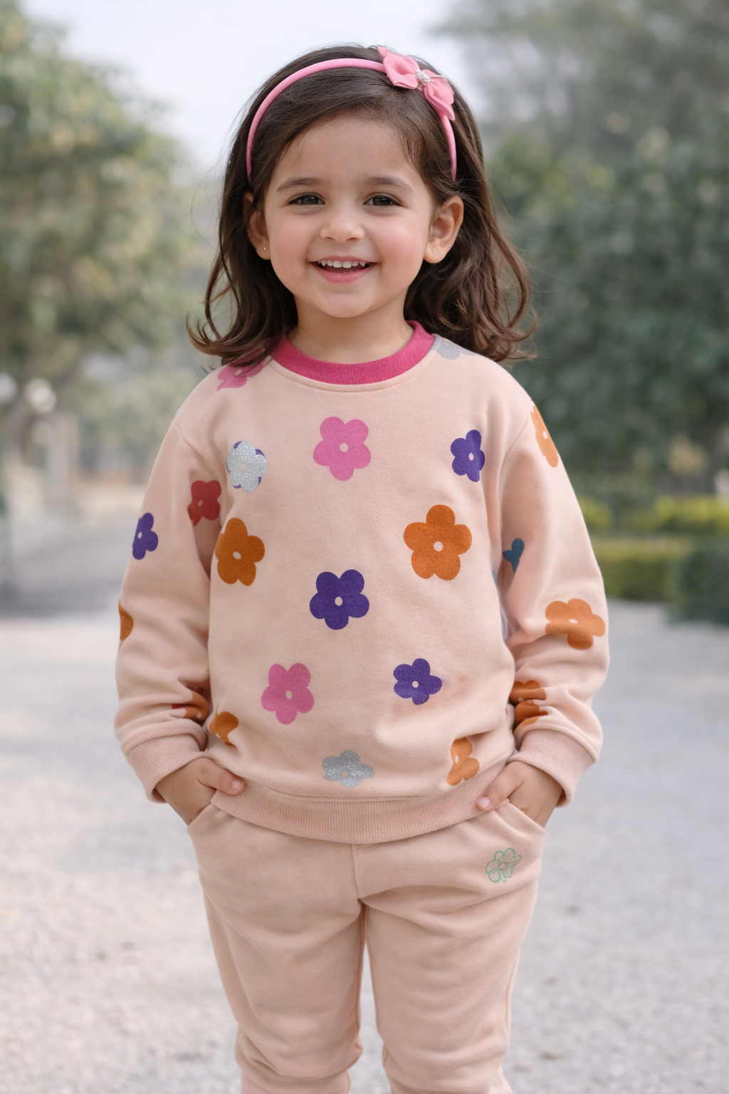 Young girl wearing a pink floral sweatshirt and pants outdoors.

