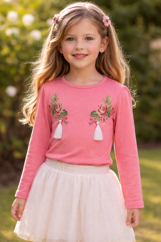 Young girl wearing a pink long-sleeve shirt with floral designs outdoors.

