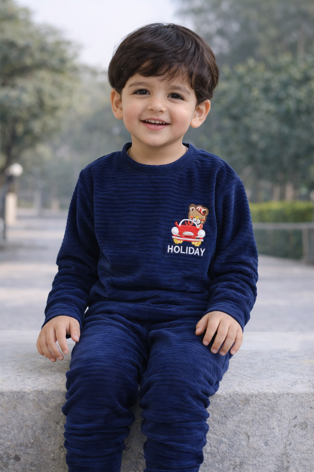 Child wearing a navy blue sweater with a logo and text, sitting outdoors.

