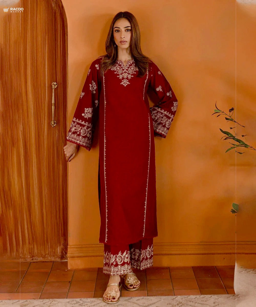 Woman wearing a red traditional outfit with white patterns against an orange wall.

