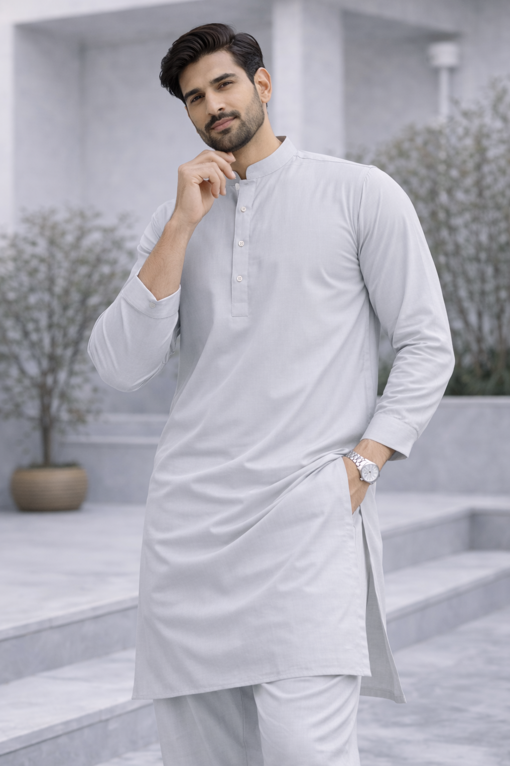 Man wearing a light gray kurta in an outdoor setting with plants and steps.

