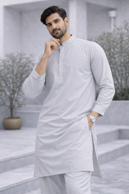 Man wearing a light gray kurta in an outdoor setting with plants and steps.

