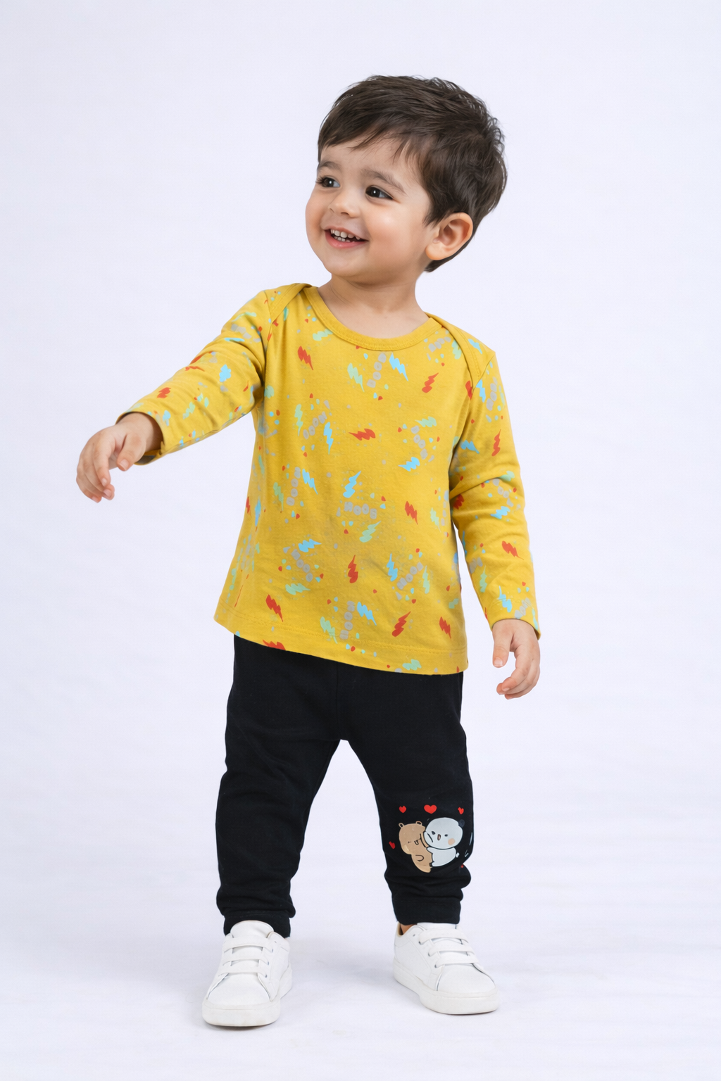 Child wearing a yellow long-sleeve shirt with colorful patterns and black pants on a white background

